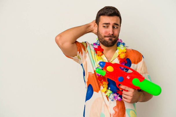Young caucasian woman on a hawaiian party holding a water gun isolated on white background touching back of head, thinking and making a choice. - Photo, image