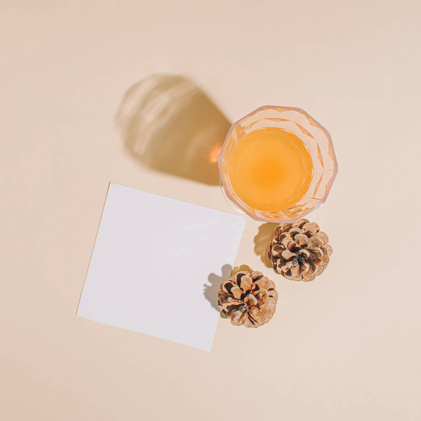 Minimal copy space flat lay arrangement with fresh pine, white card and drinking glass on pastel beige background. Creative holiday season concept, autumn and Halloween mood. - Photo, Image