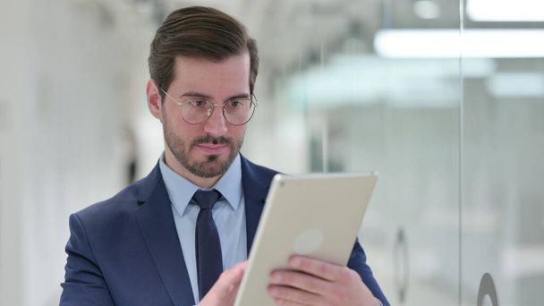 Серьезный профессиональный молодой бизнесмен, использующий планшет в офисе  - Фото, изображение
