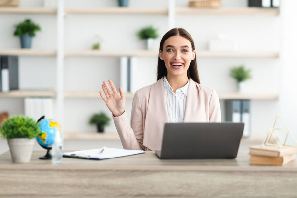 Весёлая женщина-менеджер машет "Hello Sitting at Laptop In Office" - Фото, изображение