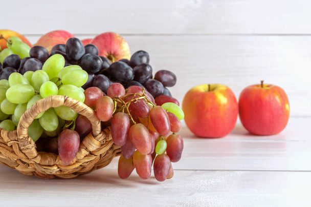 Různé odrůdy hroznů a jablek v proutěném koši na lehkém dřevěném pozadí. Kopírovat prostor. - Fotografie, Obrázek