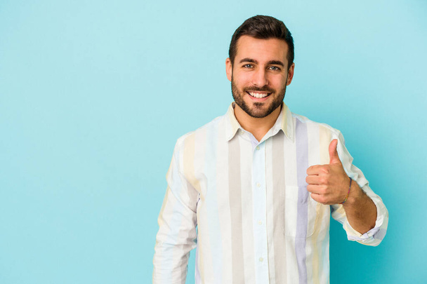 Young caucasian man isolated on blue background smiling and raising thumb up - Φωτογραφία, εικόνα