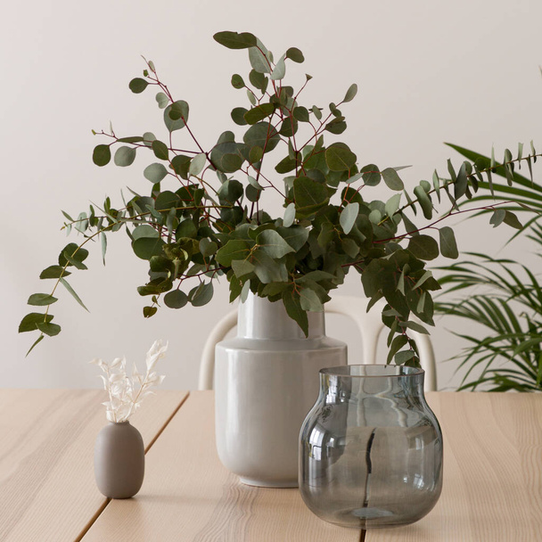 Close-up on stylish wooden table with delicate and elegant decorations, glass pot and ceramic vase with eucalyptus twigs - Foto, immagini