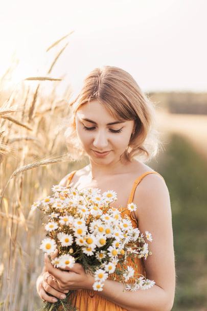 Młoda piękna dziewczyna z bukietem stokrotek na polu pszenicy - Zdjęcie, obraz