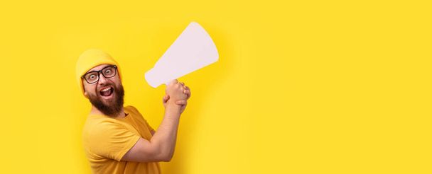 man holding megaphone over yellow background, panoramic layout with space for text - Fotoğraf, Görsel