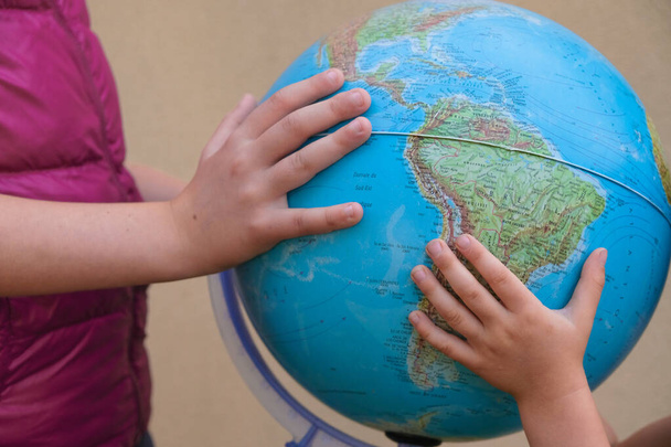 Children's hands with a globe. Siblings play with a globe. - Foto, afbeelding