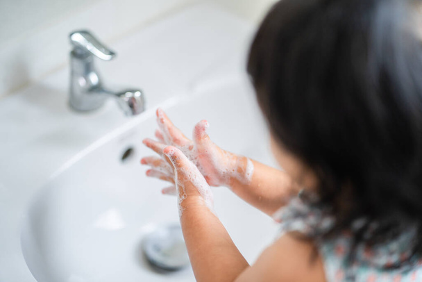A closeup shot of a little girl washing her hands in a sink in the bathroom - Фото, зображення