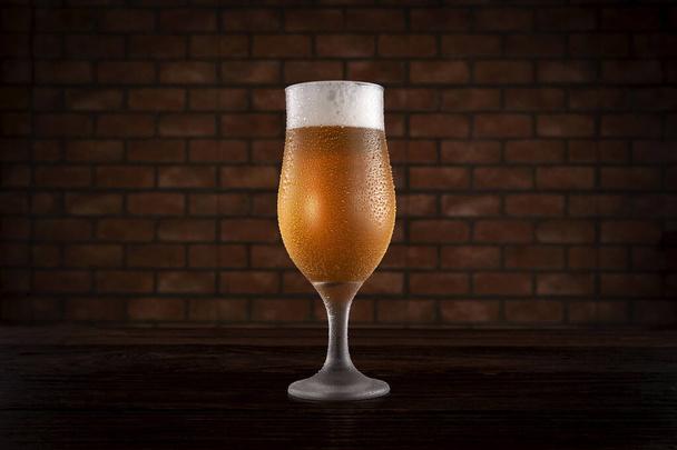Isolated sweaty tulipa glass of refreshing pilsen draft beer with brick wall background. - Photo, Image