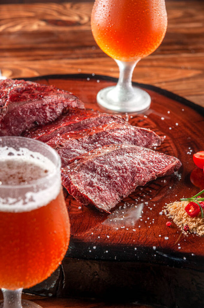 Grilled denver steak sliced on wooden cutting board with parrilla salt and two sweaty clod glasses of beer. Marble meat beef - Closeup. - Фото, зображення