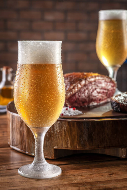 木製のまな板の上に焼きスライスキャップランプステーキとビールの汗冷たいチューリップガラス(ブラジルのpicanha). - 写真・画像