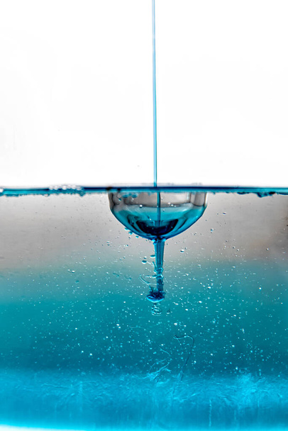 Szybki-szybka fotografia kropli na nieruchomej niebieskiej powierzchni wody - Zdjęcie, obraz