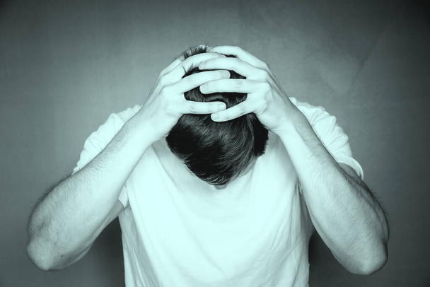 A grayscale shot of a man holding his head with his hands, feeling distraught and stressed - Foto, Imagem