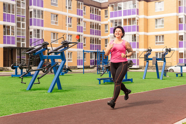 žena běhá na sportovním hřišti ve dvoře městského domu na pozadí pouličního cvičebního vybavení - Fotografie, Obrázek