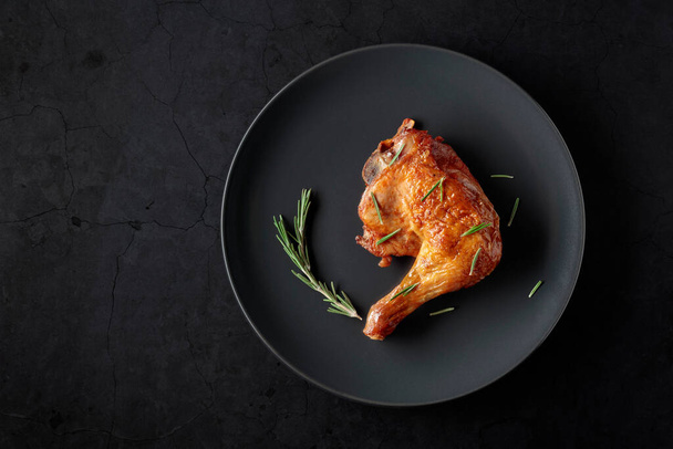 Grilled chicken leg sprinkled with rosemary on a black stone table. Top view with copy space. - Foto, afbeelding
