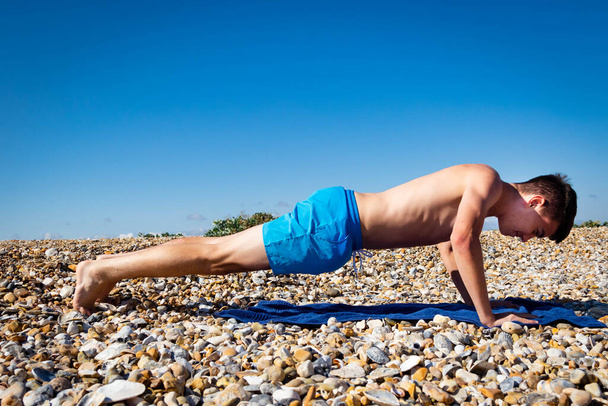 A 18 year old Caucasian teenage boy doing press ups on a stony beach  - Foto, immagini
