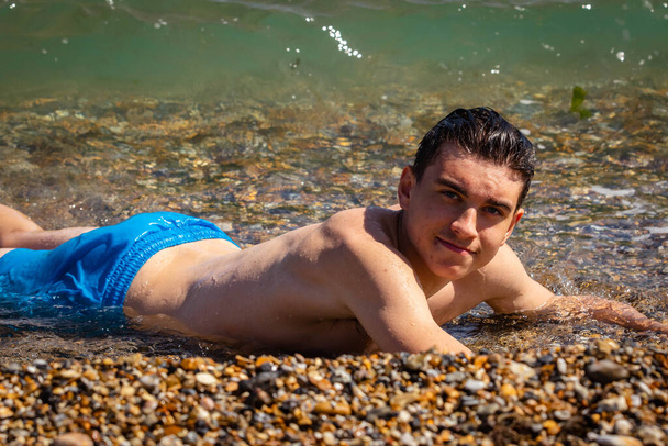 A 18 year old Caucasian shirtless teenage boy laying in the surf - Фото, зображення