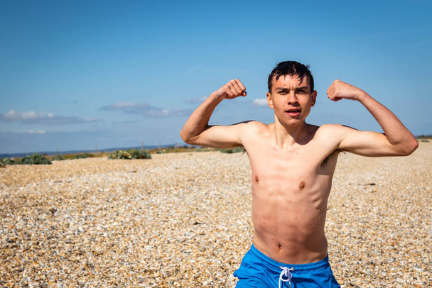 A 18 year old Caucasian shirtless teenage boy relaxing on a beach next to the sea - Φωτογραφία, εικόνα