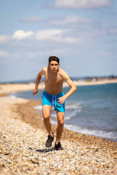 A 18 year old Caucasian shirtless teenage boy running on a beach next to the sea - Foto, Imagem