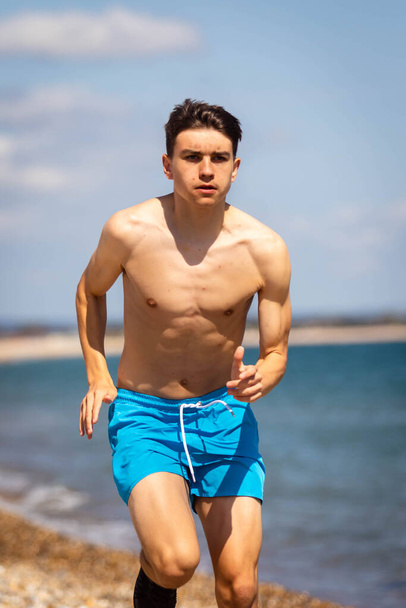 A 18 year old Caucasian shirtless teenage boy running on a beach next to the sea - Foto, Imagem