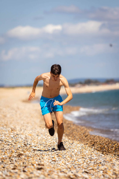 18-летний кавказский юноша без рубашки бегает по пляжу рядом с морем - Фото, изображение