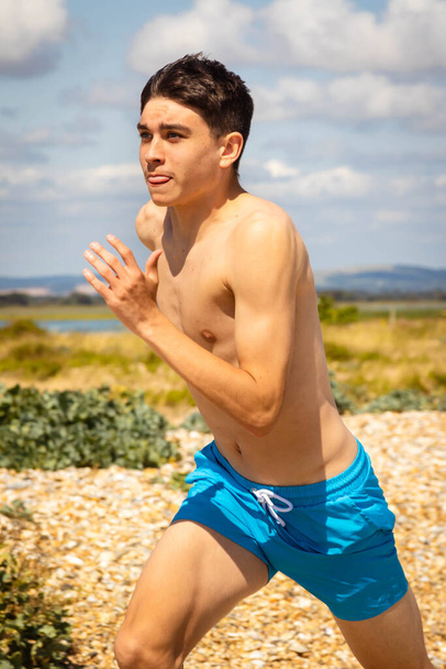 A 18 year old Caucasian shirtless teenage boy running on a beach - 写真・画像