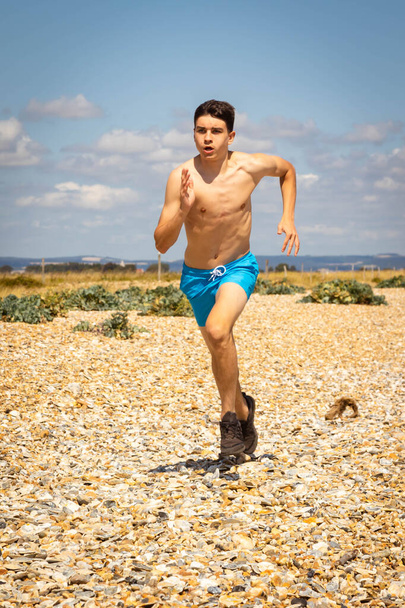 A 18 year old Caucasian shirtless teenage boy running on a beach - Foto, afbeelding