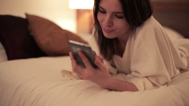 Woman with smartphone lying on bed - Filmati, video