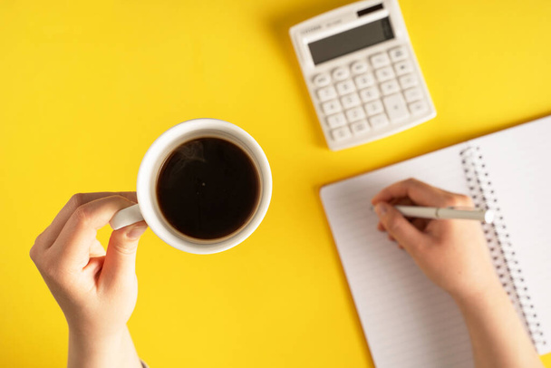 zblízka na ruce drží tužku psaní na notebooku kalkulačka na žlutém pozadí - kancelářské a obchodní plánování nebo cíle koncept přestávky na kávu - Fotografie, Obrázek