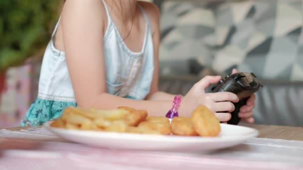 Detailní VDO show Dětská ruka nutí Joystick hrát videohry a jíst fast food, bílé jídlo s hranolky, nugety a kečup. Online zábavní technologie dělá děti závislé. - Záběry, video