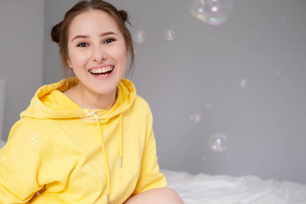 ritratto di affascinante giovane donna in giallo tra bolle di sapone su sfondo grigio brillante. adolescente alla moda. colori di tendenza - Foto, immagini