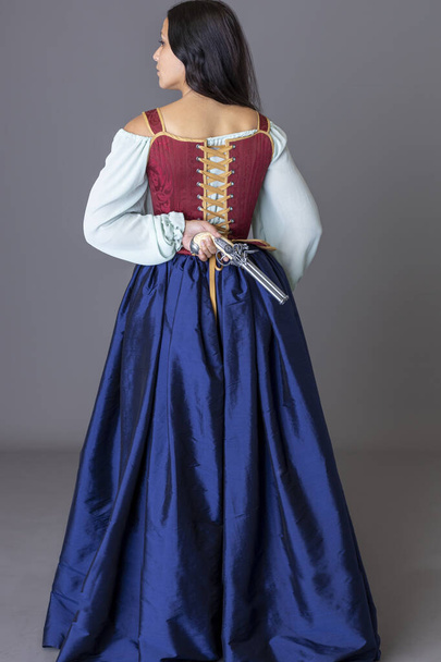 A pirate woman wearing a brocade corset and silk skirt and holding guns against a grey studio backdrop - Photo, Image