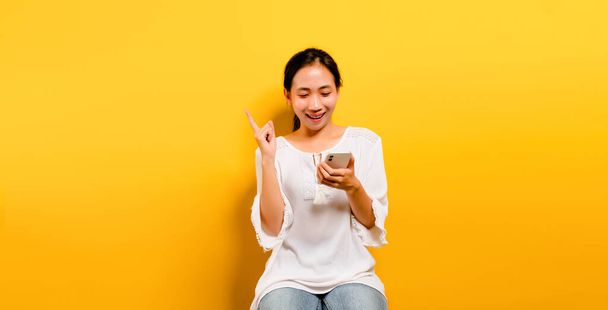 ragazza asiatica sentirsi felice e seduto e digitando su uno smartphone su uno sfondo giallo Carino ragazza asiatica sorridente in una camicia bianca. concetto di lavoro online - Foto, immagini