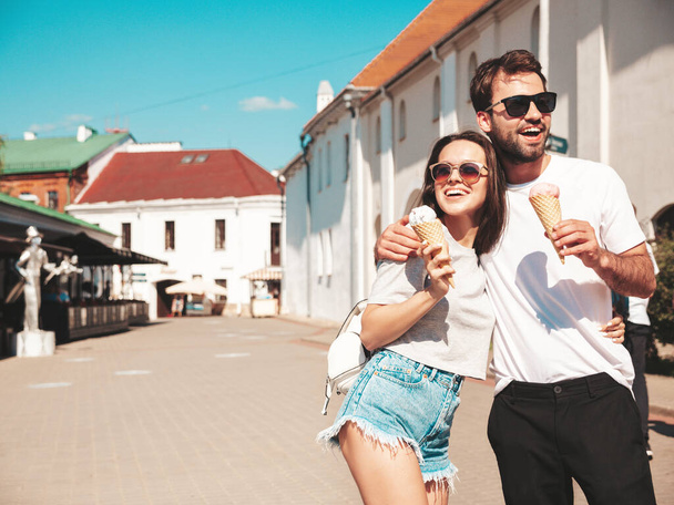 Smiling beautiful woman and her handsome boyfriend. Woman in casual summer clothes. Happy cheerful family. Couple posing on the street background in sunglasses. Eating tasty ice cream in waffles cone - Photo, image