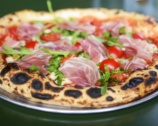 Pizza prosciutto with ham, tomato and mushrooms served on a round tray on a table inside a restaurant. Traditional Italian pizza recipe. - Valokuva, kuva