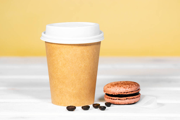 Káva jít v papírové eko šálek s čokoládou francouzský makrón na dřevěném a světle oranžovém pozadí, Rychlé občerstvení, Copyspace, Kofein Nápoj odnést - Fotografie, Obrázek