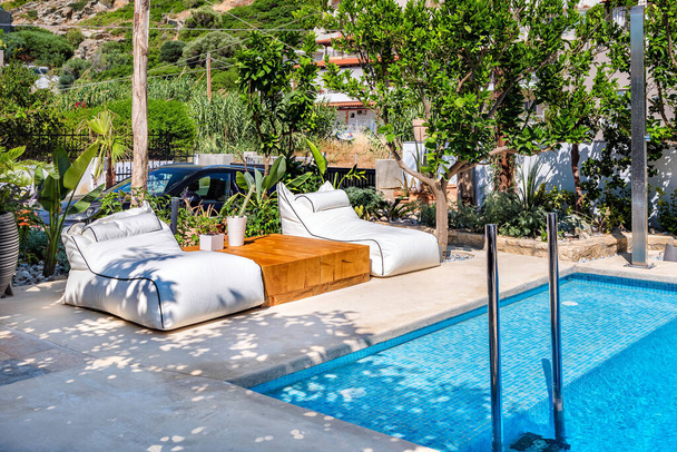 Área de relaxamento com camas macias e pequena mesa de madeira ao lado da piscina, dia ensolarado de verão, conceito de férias. - Foto, Imagem