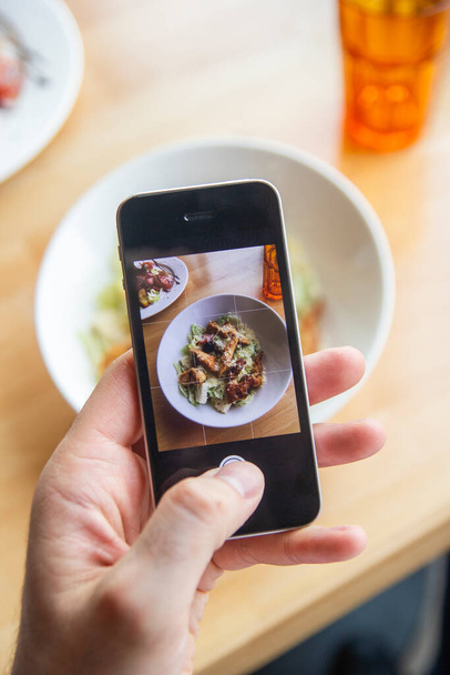 A man photographs a delicious salad on his phone in a restaurant - Fotoğraf, Görsel