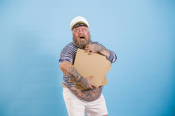 Feliz barbudo obeso marinero hombre sostiene cajas en blanco de pizza posando sobre fondo azul claro - Foto, Imagen