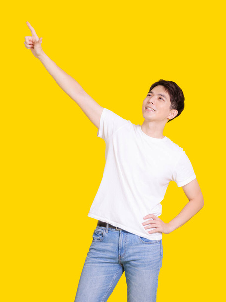 Happy handsome smiling young man with hands poiting up. Isolated on yellow background. - Photo, Image