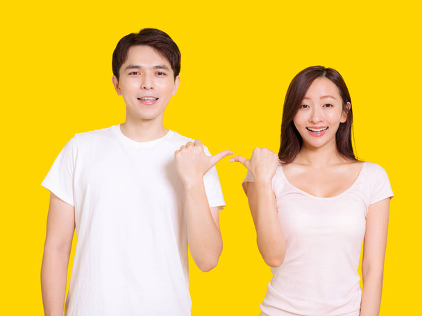 Jeune couple pointent l'un vers l'autre avec les pouces. Isolé sur fond jaune. - Photo, image