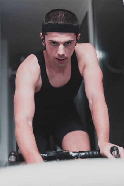 Man cycling on the machine trainer he is exercising in the home at night playing online bike racing game - Foto, Imagen