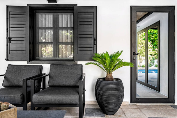 Outdoor terrace. Dark grey color armchairs, flower pot and window shutters with the white wall at the background.  - Photo, Image