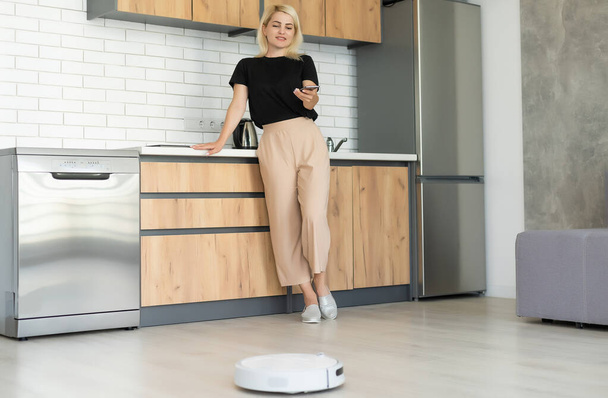 Mladá žena pomocí automatického vysavače čistit podlahu, ovládání stroje domácí práce robot - Fotografie, Obrázek