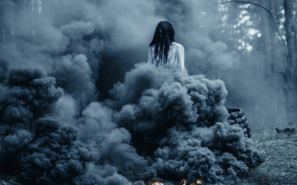 Mädchen mit langen schwarzen Haaren in Bild von beängstigenden Geist Zombie geht durch dunklen Wald vor dem Hintergrund des Rauchs. - Foto, Bild