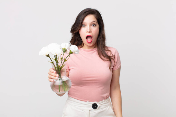 pretty woman looking very shocked or surprised and holding a decorative flowers pot - Foto, Imagen