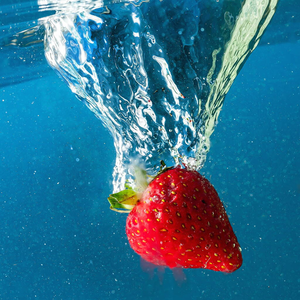 ripe strawberries fall into the water lifting splashes and air bubbles - Foto, Imagen