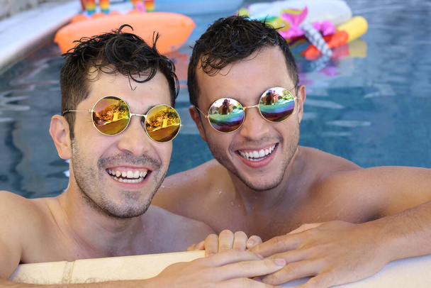 gelukkig jong gay paar met zonnebril genieten van hun tijd samen in zwembad - Foto, afbeelding