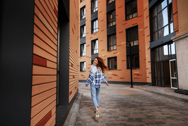 a girl in a plaid shirt runs around the city and smiles. urban style - Φωτογραφία, εικόνα