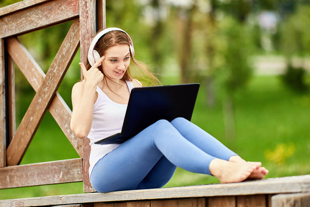 Woman in wireless headphones works using laptop outside. - Photo, Image