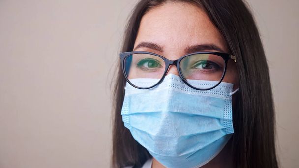 Primer plano de la joven morena doctora con gafas y máscara protectora azul claro - Foto, imagen